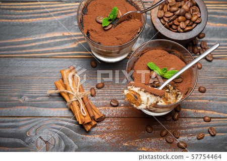 Portion of Classic tiramisu dessert in a glass and savoiardi cookies on wooden background Portion of Classic tiramisu dessert in a glass and savoiardi cookies on wooden background 57754464