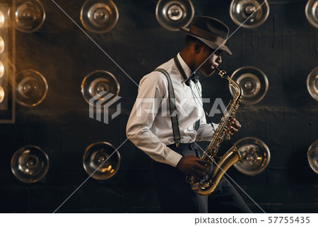 Black jazzman in hat plays the saxophone on stage 57755435