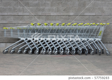Many grocery carts with yellow handles standing in a row in the centre of photo by gray brick 57759283
