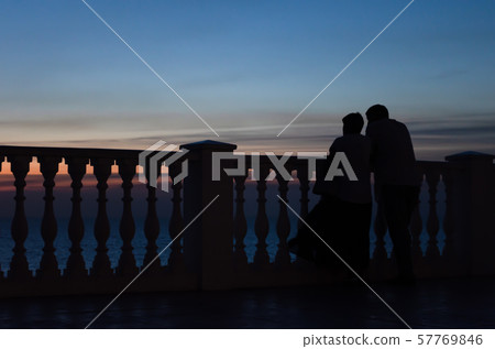 Husband and wife stand and watch the sunset by the sea near the fence of balusters 57769846