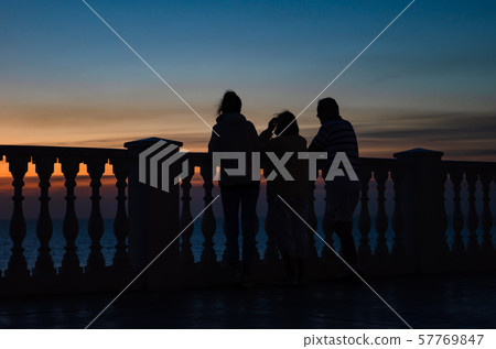 Family stand and watch the sunset by the sea near the fence of balusters 57769847