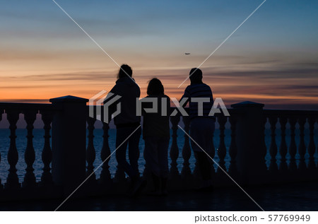 Family stand and watch the sunset by the sea near the fence of balusters 57769949