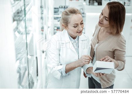 A pleasing druggist advising the female customer on vitamins ingredients A pleasing druggist advising the female customer on vitamins ingredients 57770484