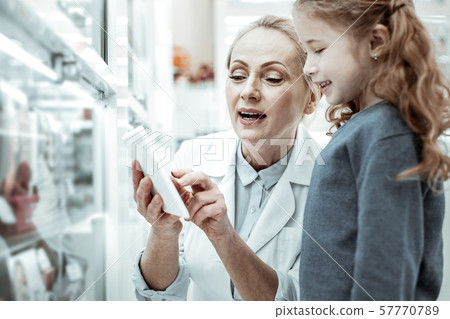 Pharmacist showing pictures of vitamins in the tablet to baby-girl Pharmacist showing pictures of vitamins in the tablet to baby-girl 57770789