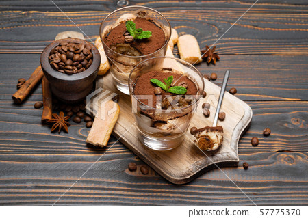 Portion of Classic tiramisu dessert in a glass and savoiardi cookies on wooden background Portion of Classic tiramisu dessert in a glass and savoiardi cookies on wooden background 57775370