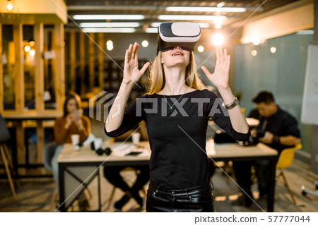Happy young woman adjusting her virtual reality headset and excited playing video game in VR device Happy young woman adjusting her virtual reality headset and excited playing video game in VR device 57777044