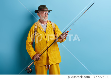old man in glasses wearing stylish yellow coat preparing rod for fishing old man in glasses wearing stylish yellow coat preparing rod for fishing 57777392