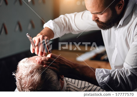 pleasant handsome stylist shaving hairs on the forehead of client pleasant handsome stylist shaving hairs on the forehead of client 57777570