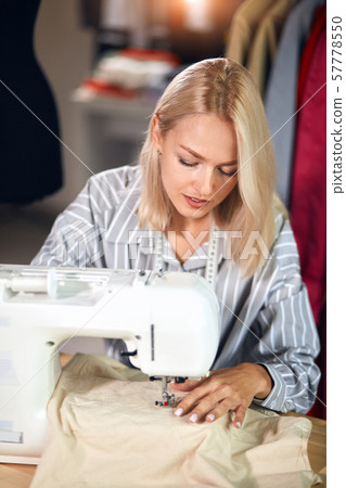 Young dressmaker sews clothes on sewing machine. small business 57778550