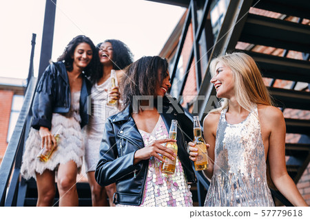 Happy women walking with bottles of beers. Young female friends having fun while stepping down stairs. 57779618