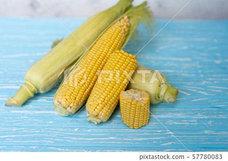 Corn cob with green leaves lies on table blue Corn cob with green leaves lies on table blue 57780083