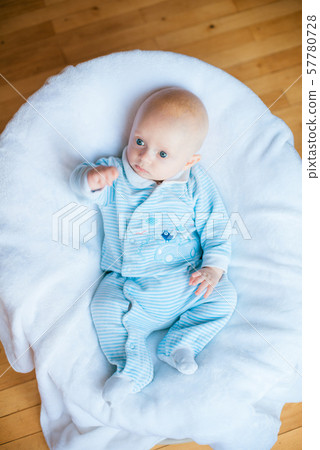 Adorable baby boy in white sunny bedroom. Newborn child relaxing in bed. Nursery for young children. Textile and bedding for kids. Family morning at home Adorable baby boy in white sunny bedroom. Newborn child relaxing in bed. Nursery for young children. Textile and bedding for kids. Family morning at home 57780728