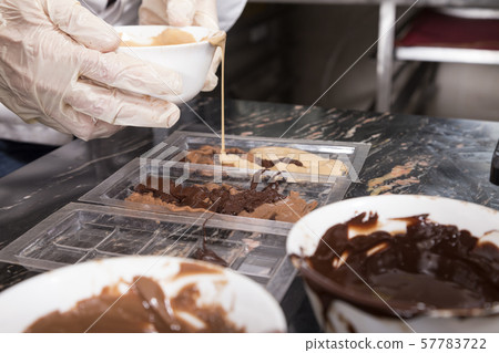 Pouring melted milk chocolate into plastic molds. 57783722