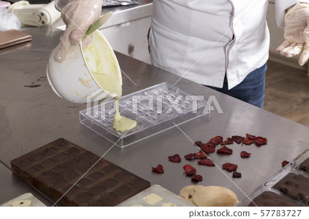 Pouring melted white chocolate into plastic molds. 57783727