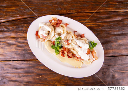 Meat and bacon pelmeni, are served with sour cream and greens 57785862