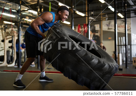 Strong African Man Flipping Tire in Gym 57786011