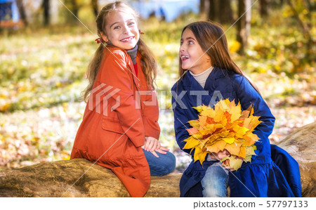 Two cute smiling 8 years old girls chatting in a park on a sunny autumn day. Two cute smiling 8 years old girls chatting in a park on a sunny autumn day. 57797133