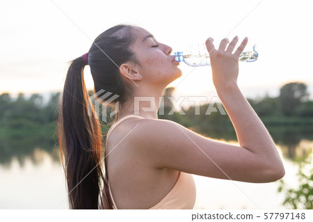 Woman athlete takes a break, she drinking water, out on a run on a hot day Woman athlete takes a break, she drinking water, out on a run on a hot day 57797148