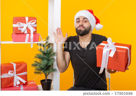 Young handsome man in a Santa Claus hat is holding congratulatory gifts next to a Christmas tree Young handsome man in a Santa Claus hat is holding congratulatory gifts next to a Christmas tree 57801686