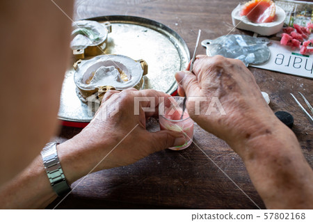 Dentures processing set concept, Senior man's hand making Artificial teeth, Dental prosthesis on wood background 57802168