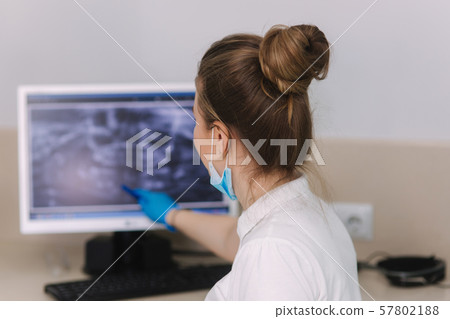 Young female dentist sitting by the monitor with x-ray 57802188