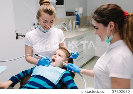 Children's dentist and assistant examination boy's teeth, while he sitting on the dental chair at Children's dentist and assistant examination boy's teeth, while he sitting on the dental chair at 57802680
