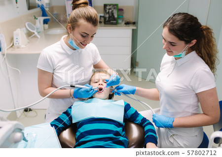 Children's dentist and assistant examination boy's teeth, while he sitting on the dental chair at Children's dentist and assistant examination boy's teeth, while he sitting on the dental chair at 57802712