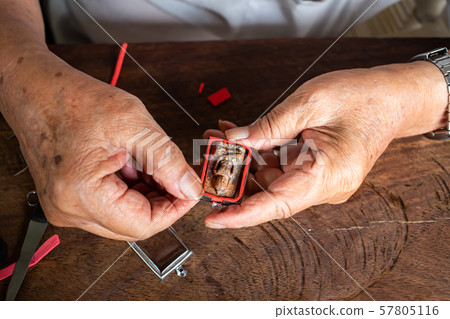 Senior man's hands to provide Amulet, Small Buddha image with a metal cap on wood table texture background, Close up & Macro shot, Asian body part, Craftsman processing concept 57805116