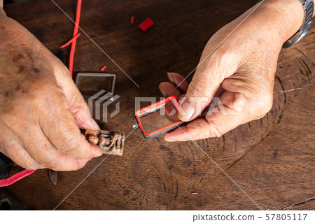 Senior man's hands to provide Amulet, Small Buddha image with a metal cap on wood table texture background, Close up & Macro shot, Asian body part, Craftsman processing concept 57805117