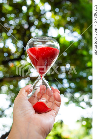 Woman's left hands holding red hourglass in bokeh green garden background, Close up & Macro shot, Selective focus, Time concept Woman's left hands holding red hourglass in bokeh green garden background, Close up & Macro shot, Selective focus, Time concept 57806215