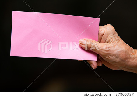 Senior woman's right hand holding pink envelope in bokeh black colour background, Close up shot, Business concept Senior woman's right hand holding pink envelope in bokeh black colour background, Close up shot, Business concept 57806357