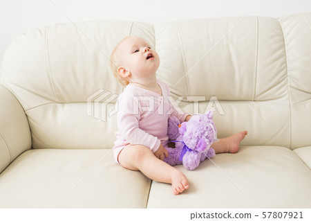 childhood, babyhood and people concept - happy little baby girl sitting on couch at home 57807921