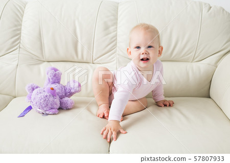 childhood, babyhood and people concept - happy little baby girl sitting on couch at home 57807933