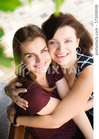 close up portrait of mother and daughter hugging on a bench in the park 57809086