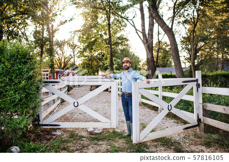 A portrait of farmer walking outdoors on family farm, opening gate. 57816105