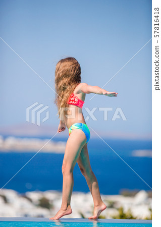 Adorable little girl on the edge of outdoor swimming pool with beautiful view 57816418