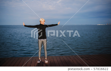 Side view portrait of young sportswoman standing outdoors on beach, stretching. Side view portrait of young sportswoman standing outdoors on beach, stretching. 57816622
