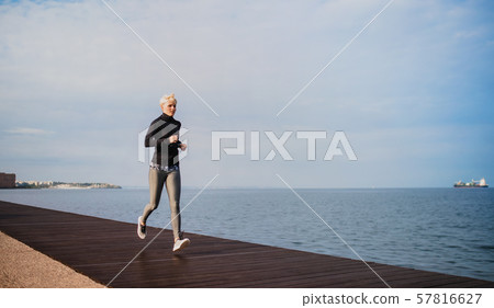 Side view of young sportswoman running outdoors on beach. Side view of young sportswoman running outdoors on beach. 57816627