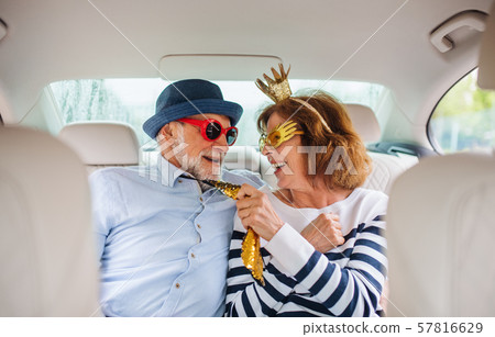 Cheerful senior couple with party accessories sitting in car, having fun. Cheerful senior couple with party accessories sitting in car, having fun. 57816629