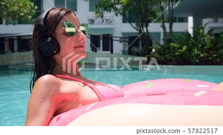 Happy woman and inflatable swim ring in the shape of a donut in the pool and listens to music at the Happy woman and inflatable swim ring in the shape of a donut in the pool and listens to music at the 57822517