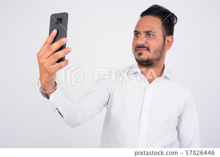 Studio shot of bearded Indian businessman taking selfie with phone 57826446