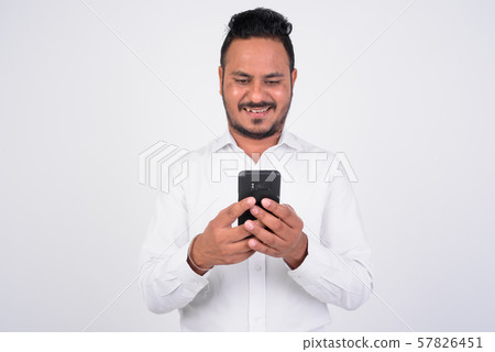 Studio shot of happy bearded Indian businessman using phone 57826451