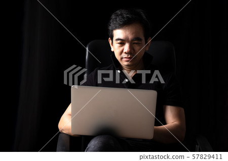40s Asian businessman sitting and looking at laptop with smiling on black background 40s Asian businessman sitting and looking at laptop with smiling on black background 57829411