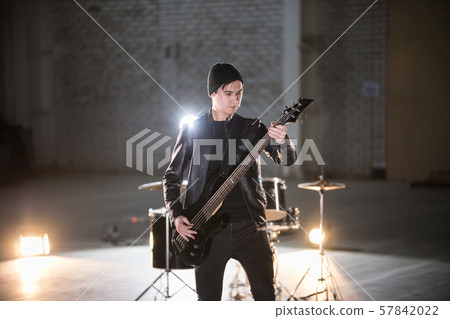 A musician man holding guitar and playing it on the background of a drum-kit 57842022
