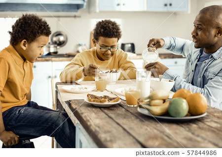 Dad preparing breakfast for his sons and finally sitting down to eat with them.