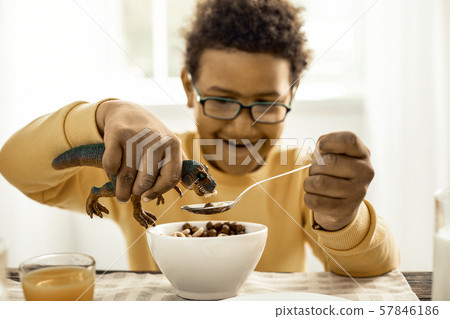Boy feeding his toy tyrannosaur with a full spoon. 57846186