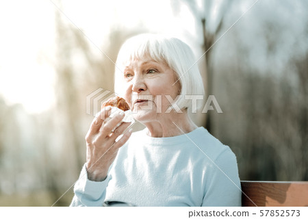 Nice smiling aged madam savoring of a delicious bun outdoor 57852573