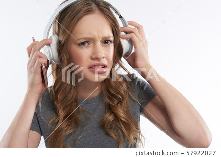 Displeased teen girl in wireless headphones biting bottom lip Displeased teen girl in wireless headphones biting bottom lip 57922027