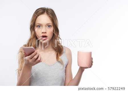 Shocked teen girl holding pink cellphone and cup of coffee Shocked teen girl holding pink cellphone and cup of coffee 57922249