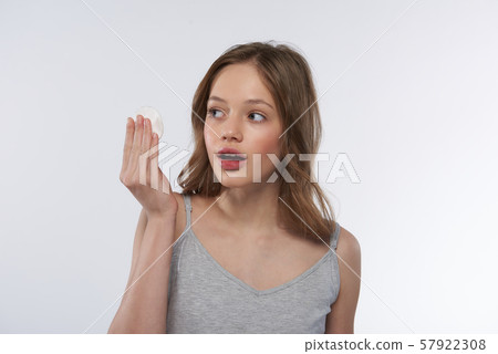Cute teen girl with cotton pad standing against white background Cute teen girl with cotton pad standing against white background 57922308